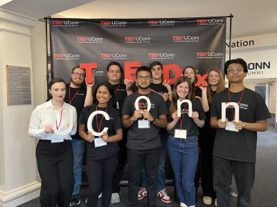 TEDxUConn Team holding letters that spell "TEDxUConn" in front of black backdrop